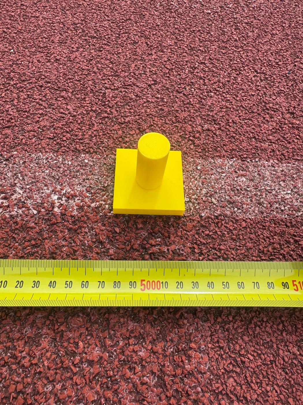 The printed yellow calibration cone sitting on a white lane line, with a tape measure alongside for scale.