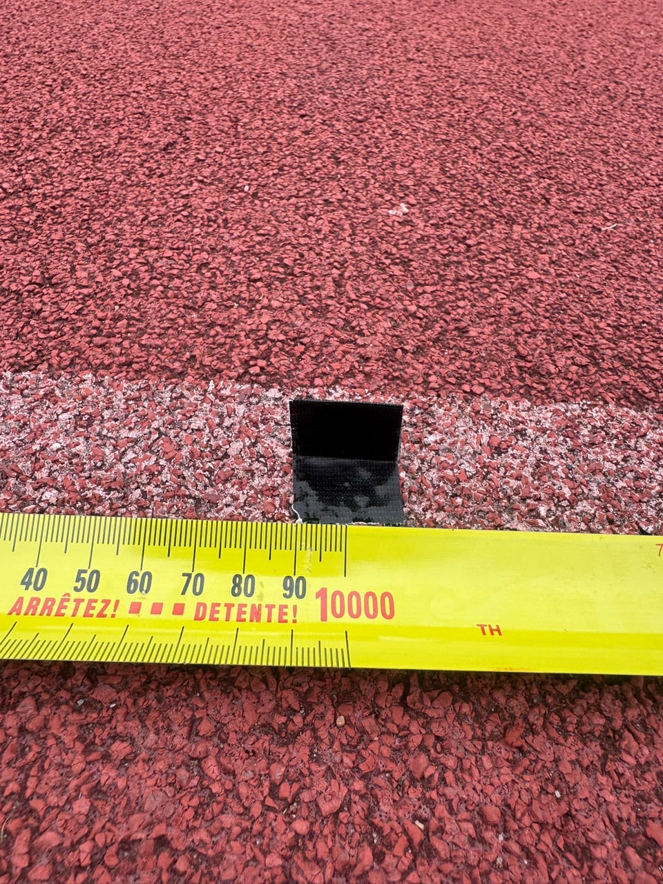 A small tape marker laid flat on the lane line, with a tape measure alongside for scale.